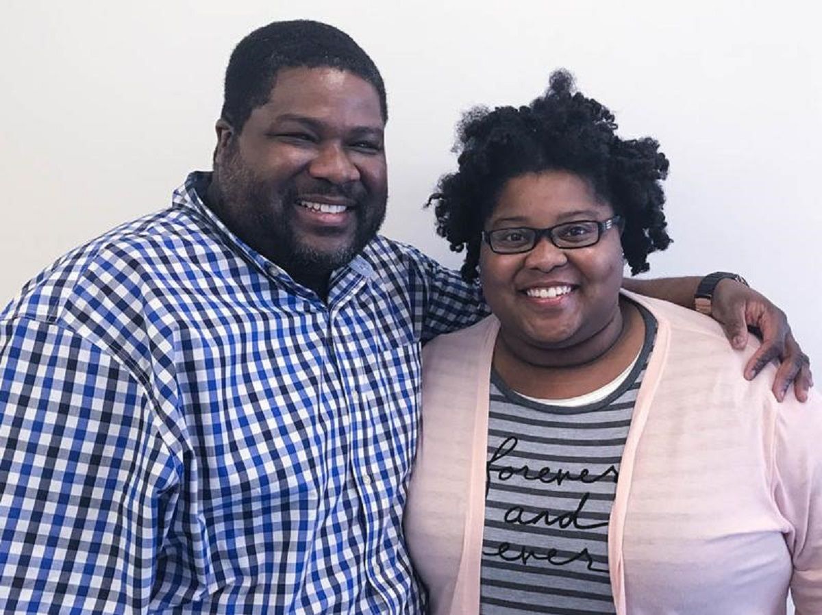 Father and daughter Edward Cage and Nicole Paris. Edward is a Black man with close-cropped hair and an incoming beard. He's wearing a blue black and white gingham print buttondown and has his arm around his daughter's shoulder. Nicole is a young Black woman with her natural hair sticking out in twists. She wears black-rimmed glasses and a black and grey striped t-shirt that reads "forever and ever" in cursive under a light pink cardigan. They're both fat, and they're both smiling. 