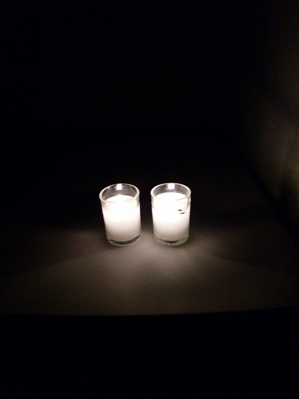Image of two lit yahrzeit candles sitting in the darkness.
