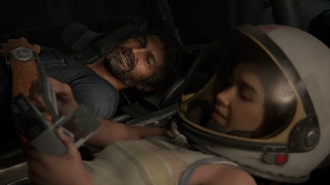 Joel and Ellie laying back in a NASA rover in a museum. In the foreground, Ellie is wearing a space helmet and a tank top as she smiles at the gift of a cassette tape for her Walkman. Joel smiles in the seat next to her. He has dark hair and a salt-and-pepper beard and a blue t-shirt. Sarah's watch is visible on his wrist.