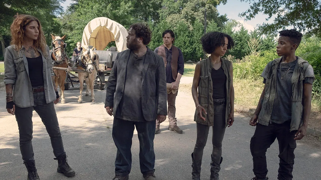 Magna (Nadia Hilker), Luke (Dan Fogler), Connie (Lauren Ridloff), and Kelly (Angel Theory) in a scene from 'The Walking Dead' They are standing in a line in the middle of a road in front of a wagon being pulled by horses.