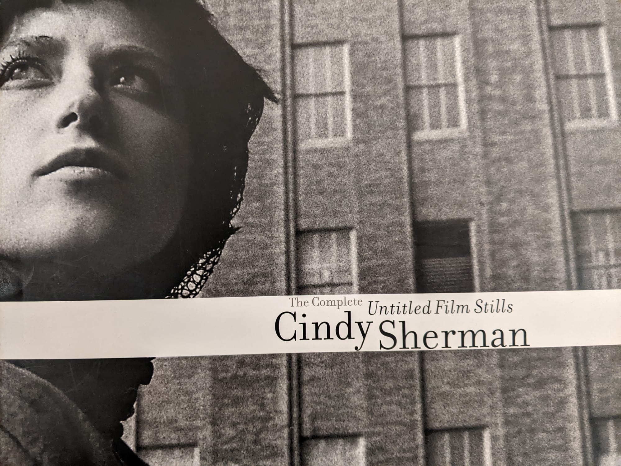 Image: a white woman with short, dark hair standing in front of a building. Title is on a white horizontal stripe.