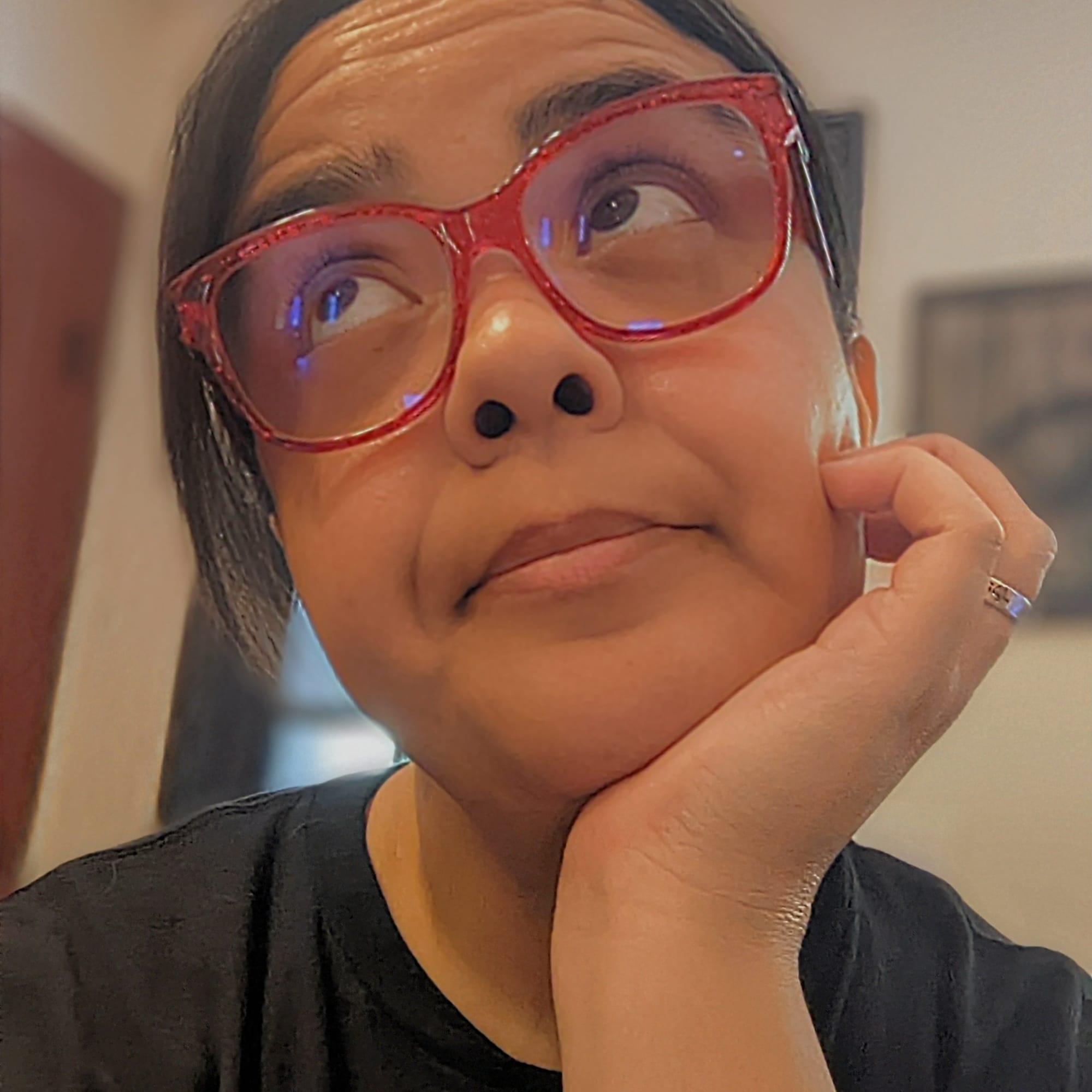 Close-up of a Latina with dark hair in a ponytail red glasses and a black t-shirt.