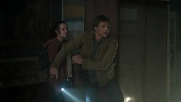 Bella Ramsey (Ellie) and Pedro Pascal (Joel) in 'The Last of Us.' Joel walks ahead of Ellie to protect her from something.