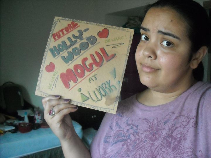 Image of me holding up a sign I made when I was 10 that reads "Future Hollywood Mogul at Work!"